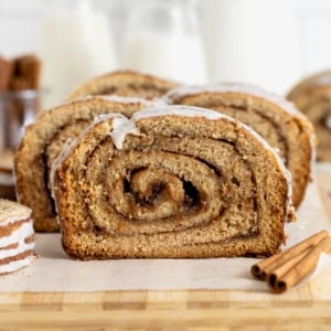 A loaf of cinnamon roll bread sliced on a parchment lined wooden cutting board.