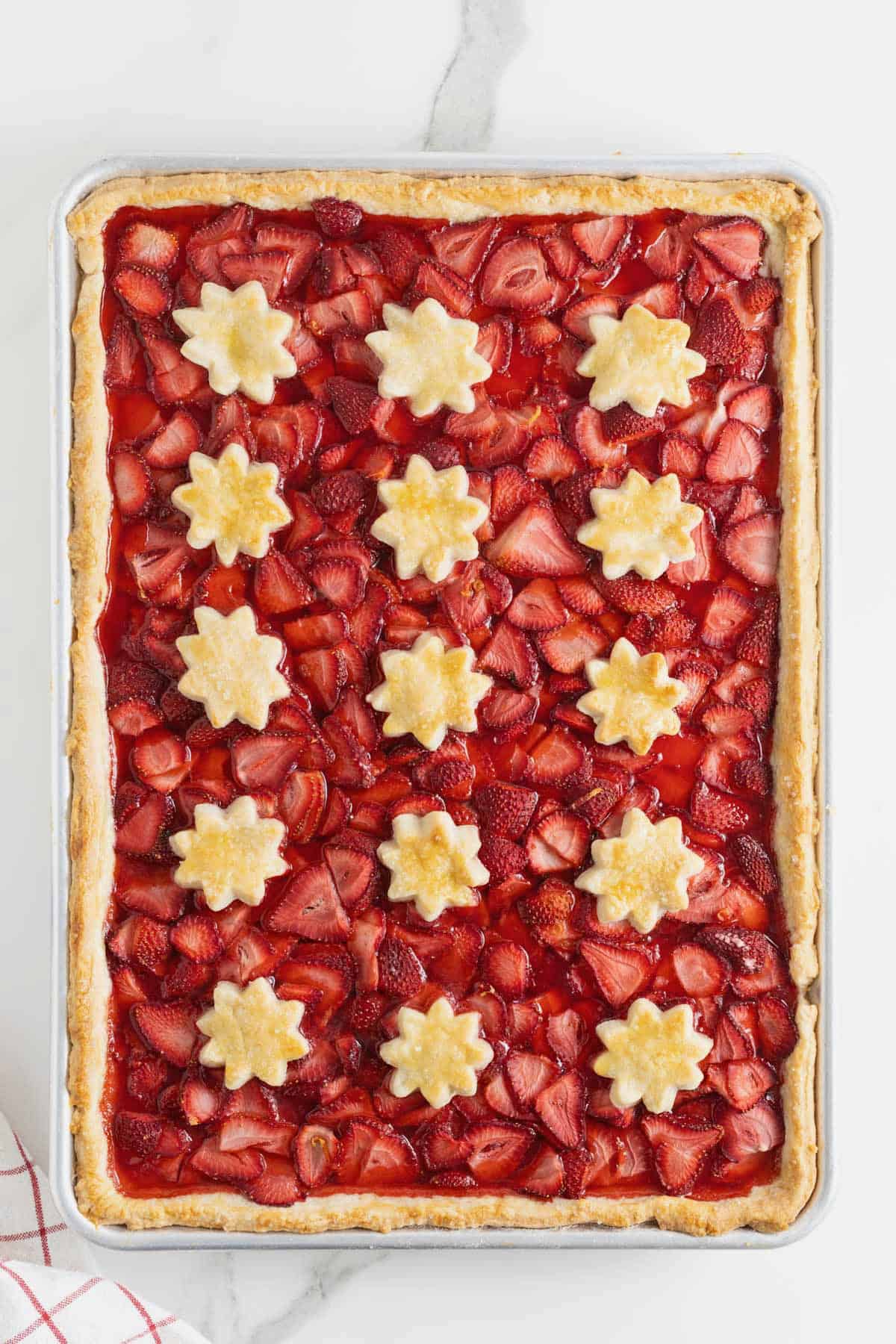 A strawberry slab pie on a white marble counter.
