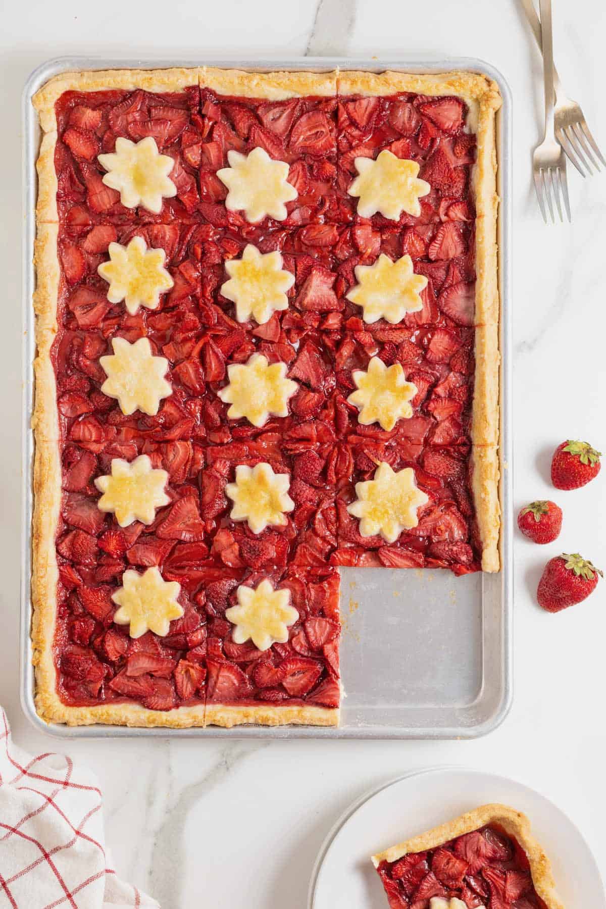 A strawberry slab pie with a piece cut out of it.