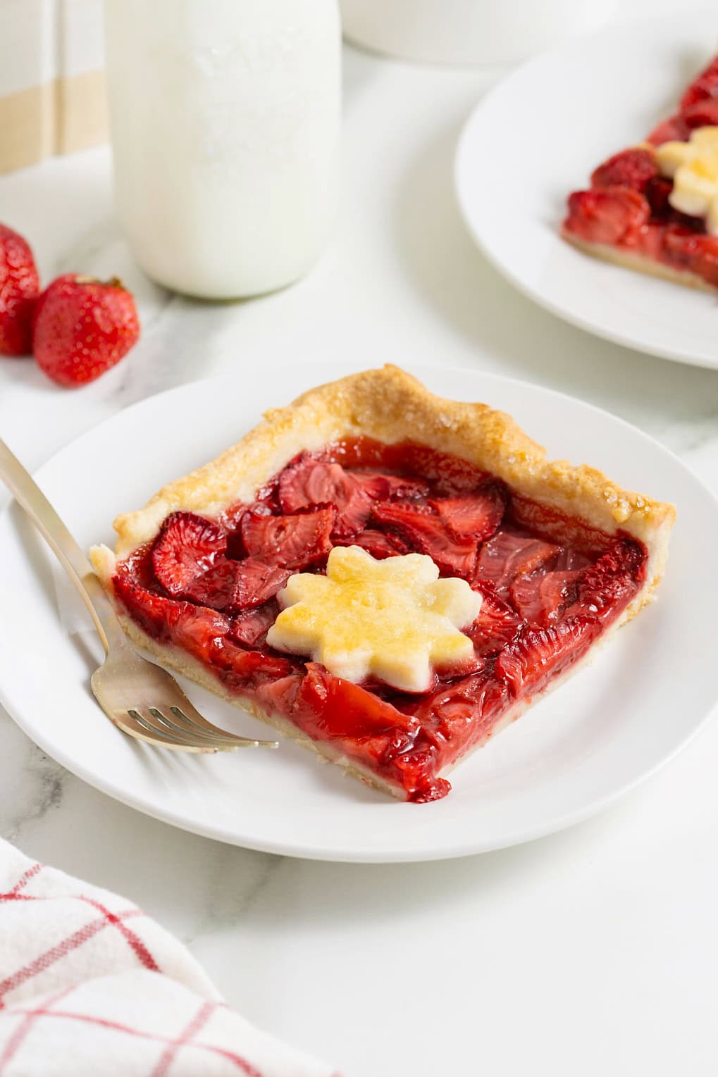 A piece of strawberry slab pie on a small white plate with a gold-toned fork.