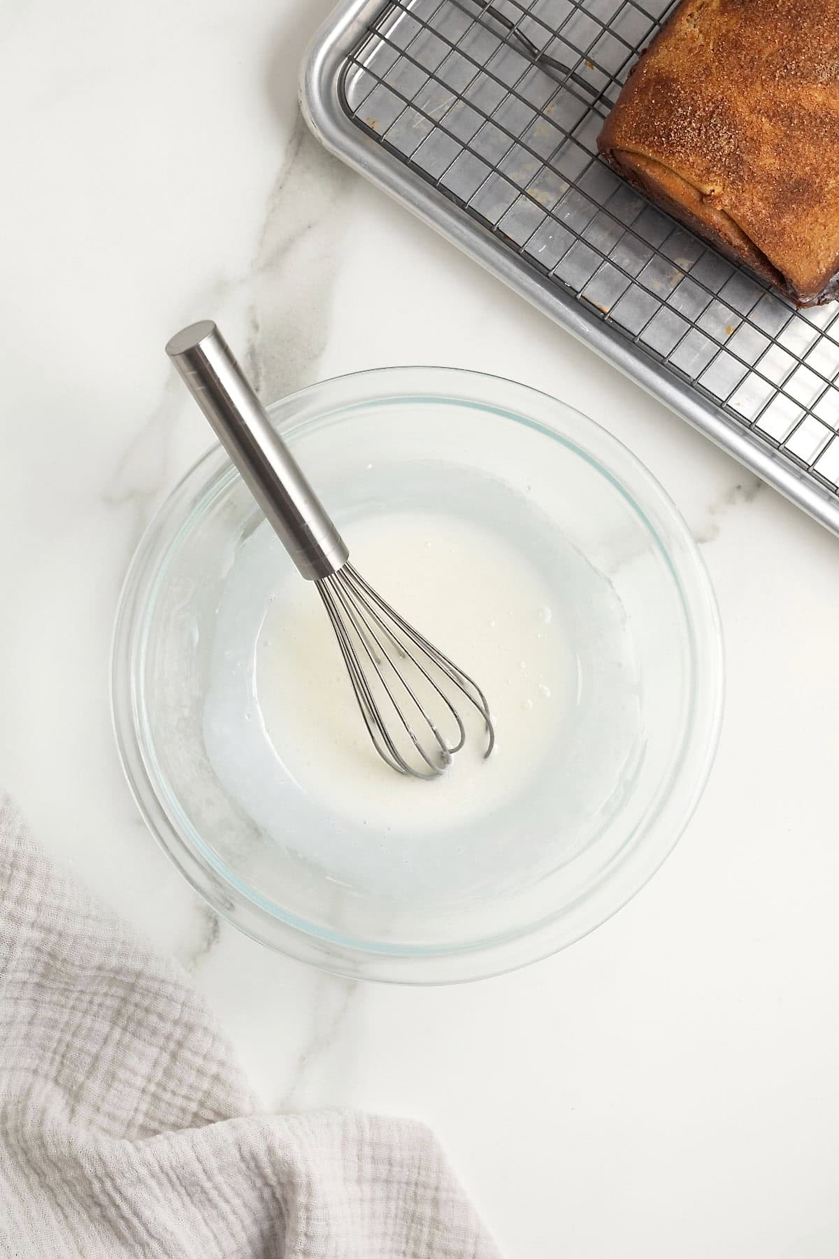 A whisk in a glass bowl of white glaze.