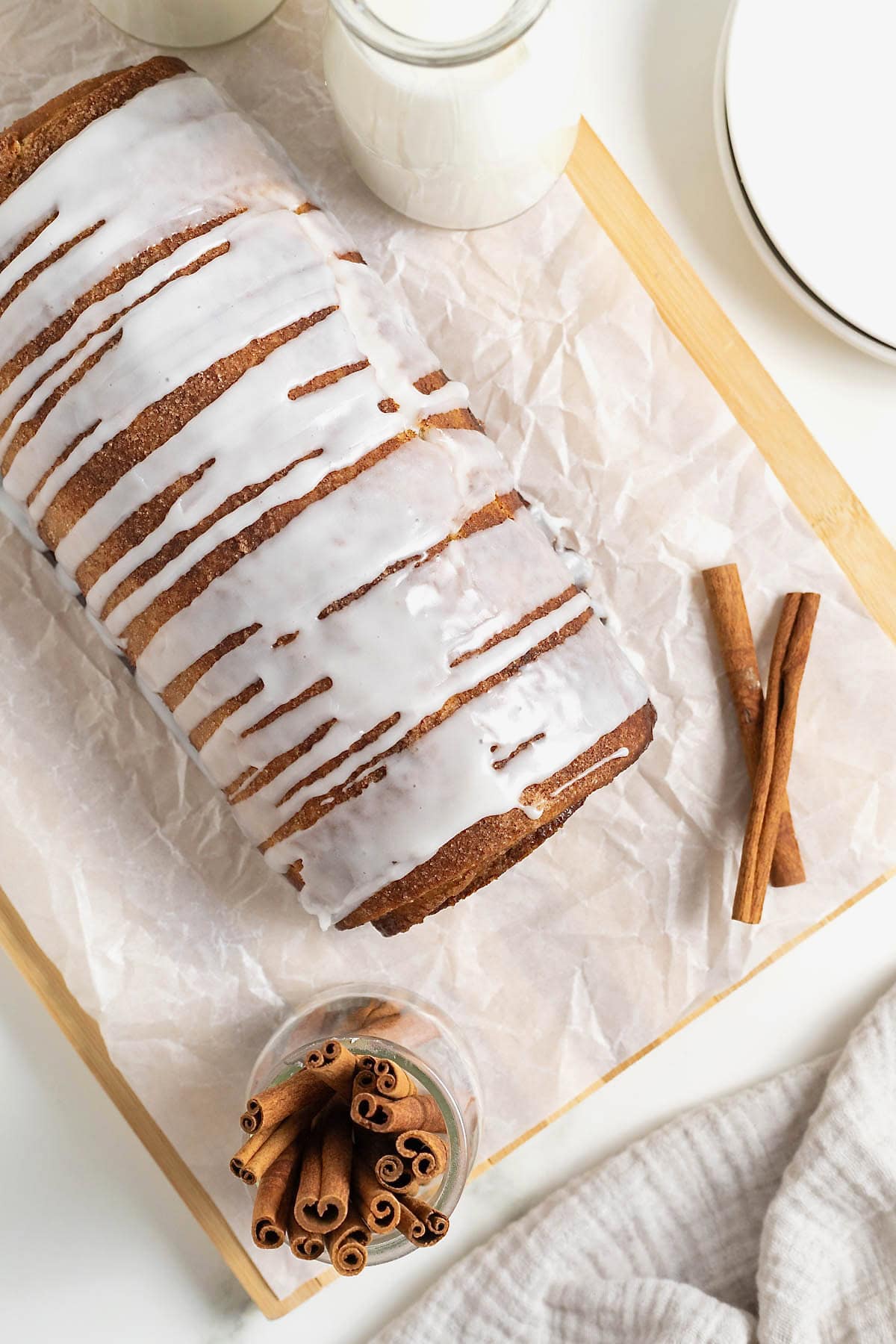 A loaf of cinnamon roll bread on a light colored wood cutting board.