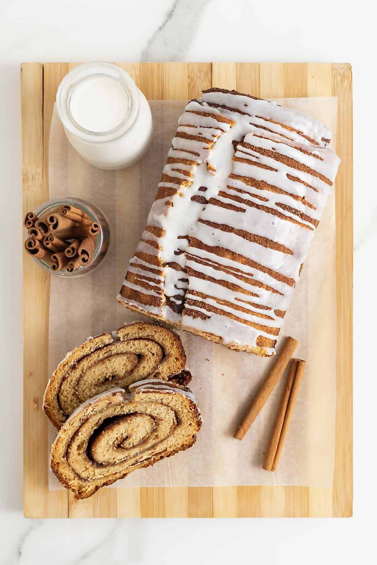 A loaf of cinnamon roll bread on a light colored wood cutting board.