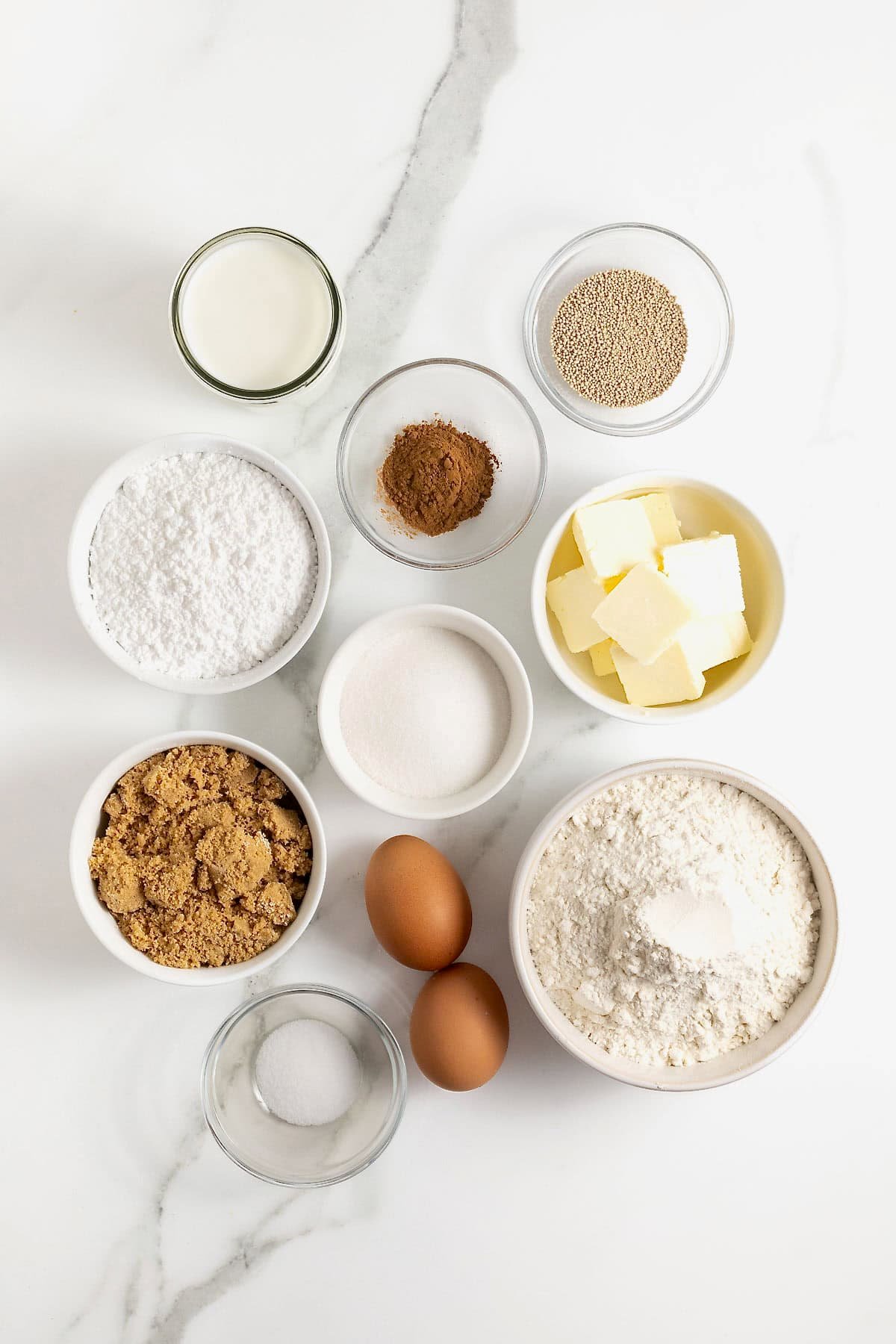Ingredients to make cinnamon roll bread in small glass dishes on a white marble counter.