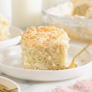 A slice of coconut cream sheet cake on a rimmed white dessert plate.