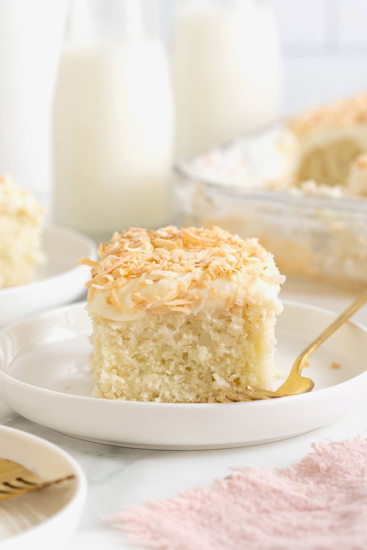 A slice of coconut cream sheet cake on a rimmed white plate.