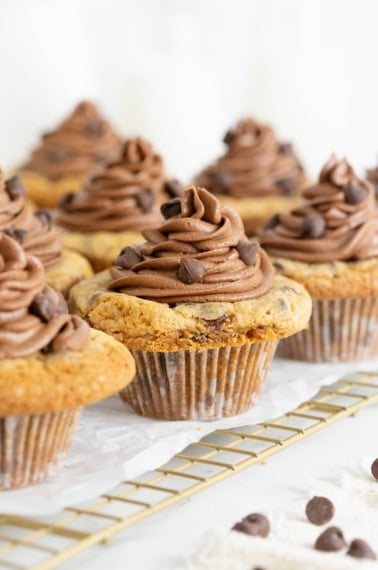 Eight cookie cup cupcakes on a parchment lined wire cooling rack.