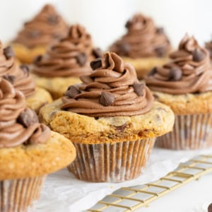 Eight cookie cup cupcakes on a parchment lined wire cooling rack.