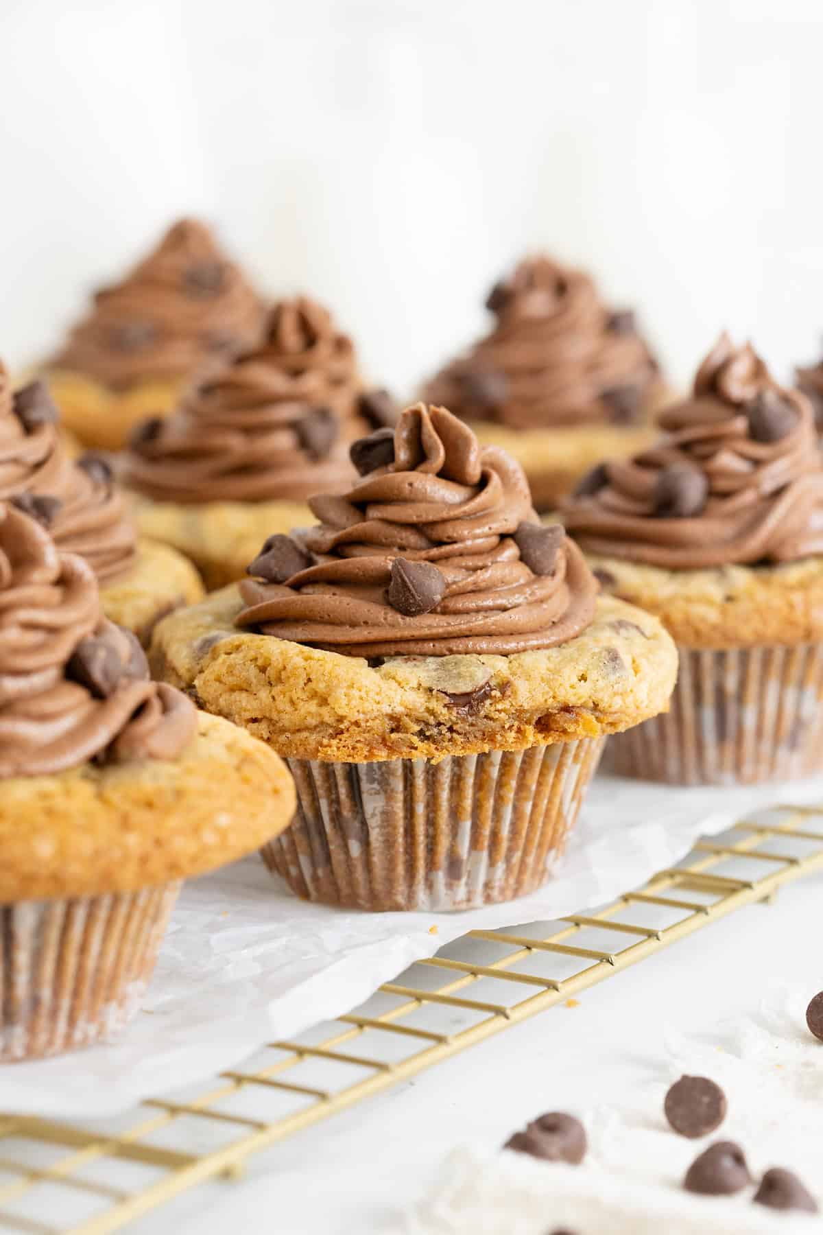Eight cookie cup cupcakes on a parchment lined wire cooling rack.