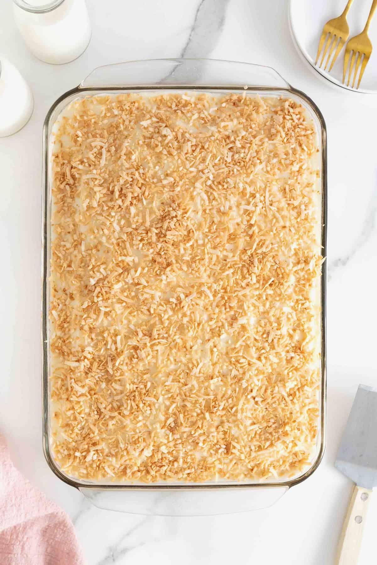 A coconut cream sheet cake in a glass baking dish on a white marble counter.