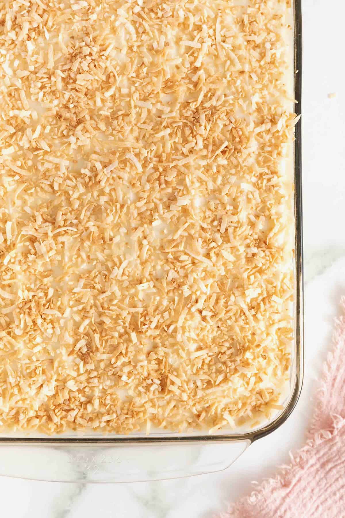 A coconut cream sheet cake in a glass baking dish on a white marble counter.