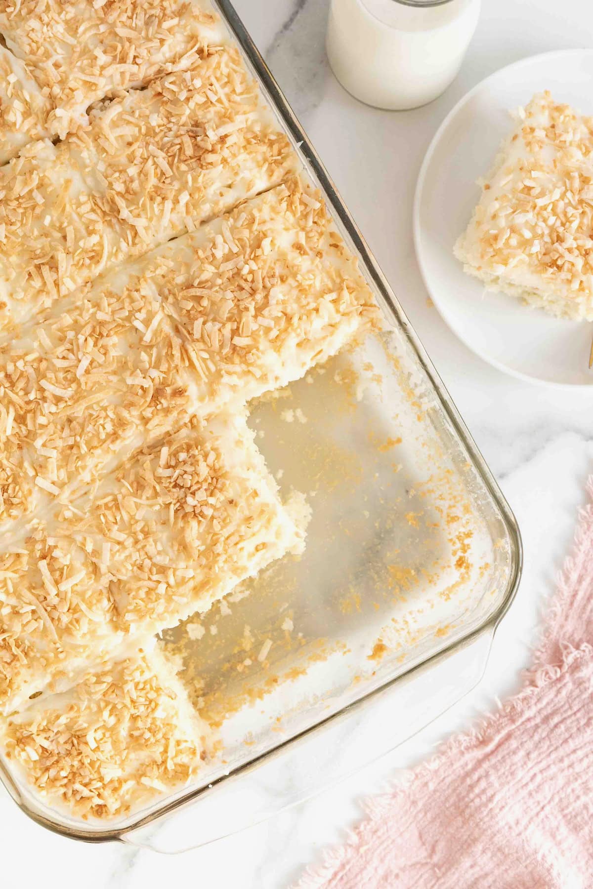 A coconut cream sheet cake in a glass baking dish with several slices removed.