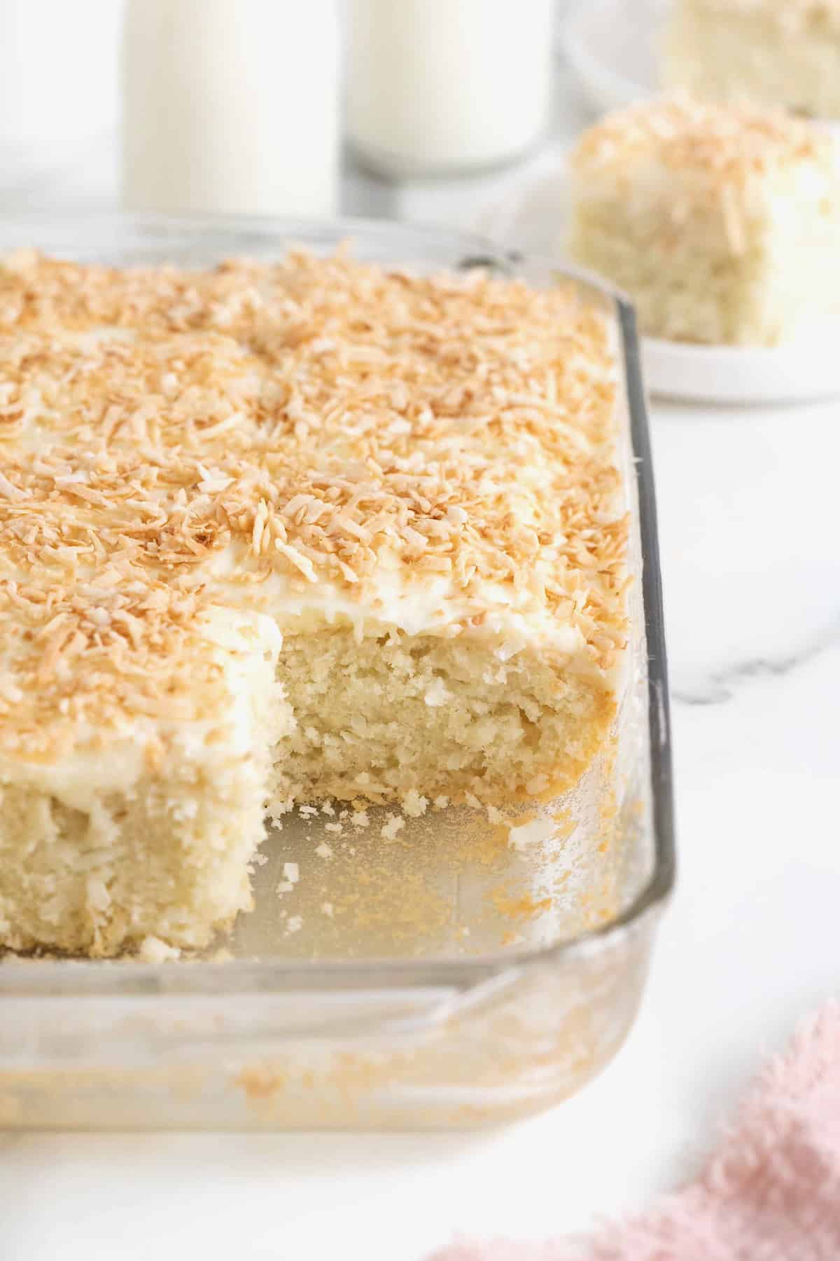 A coconut cream sheet cake in a glass baking dish with several slices removed.