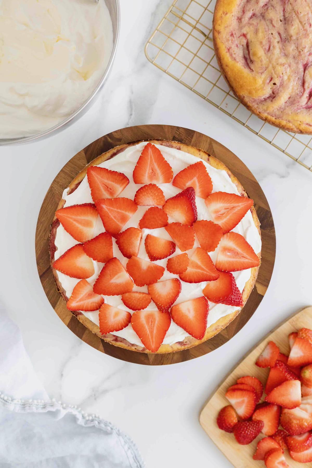 Sliced strawberries arranged on top of a layer of whipped cream frosting spread on a layer of vanilla cake.
