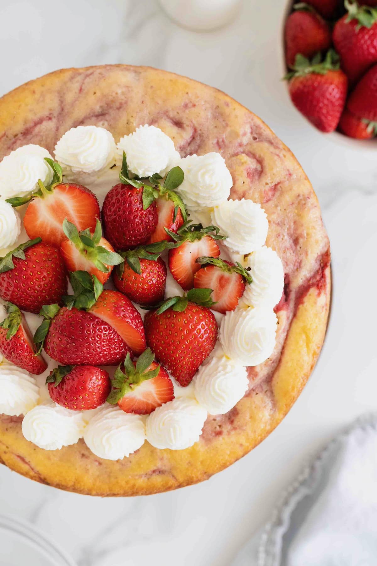 A vanilla cake with strawberry swirls topped with whipped cream and strawberries.