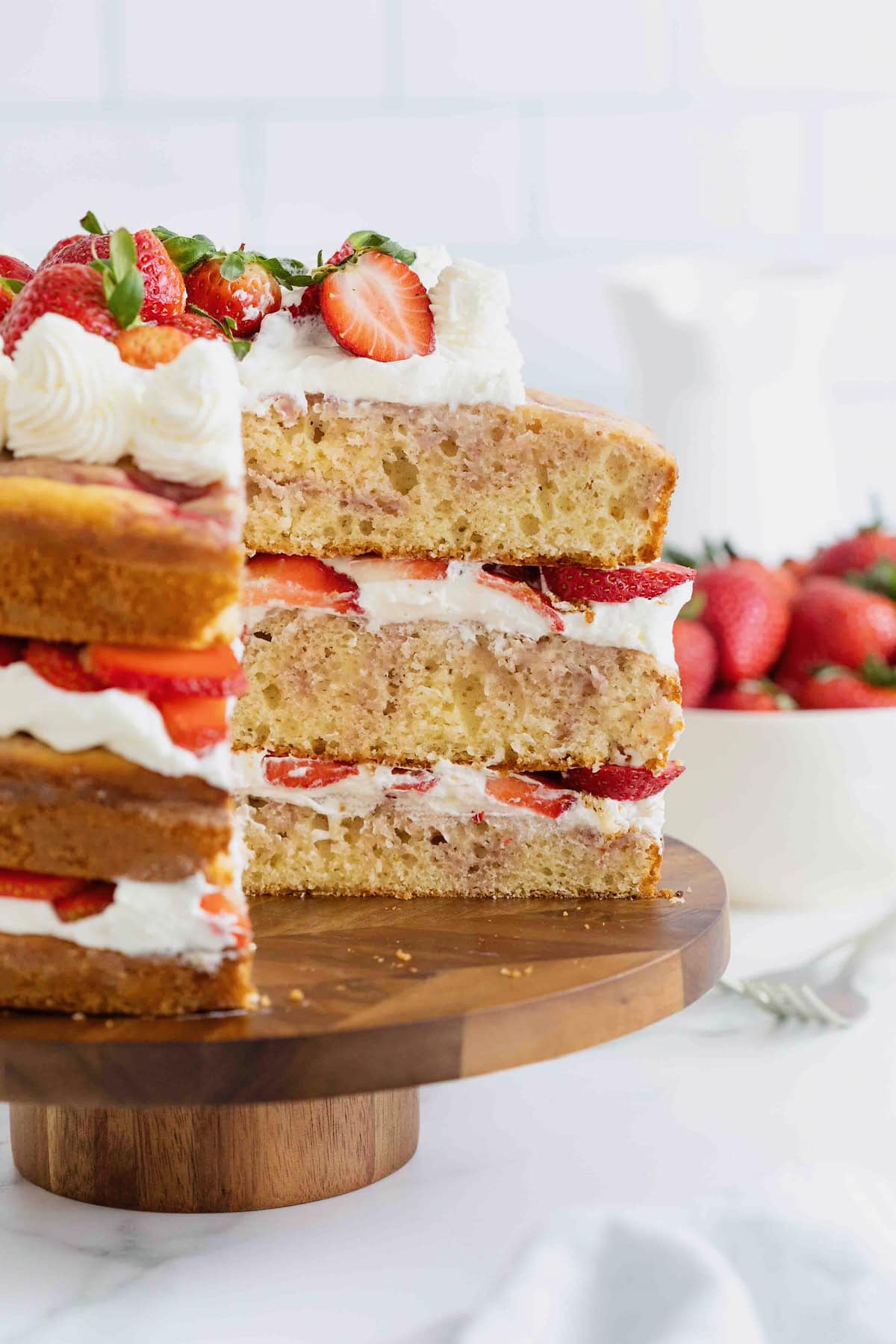 A three layer cake with strawberry swirls on a wooden cake stand. A slice has been cut out of the cake.