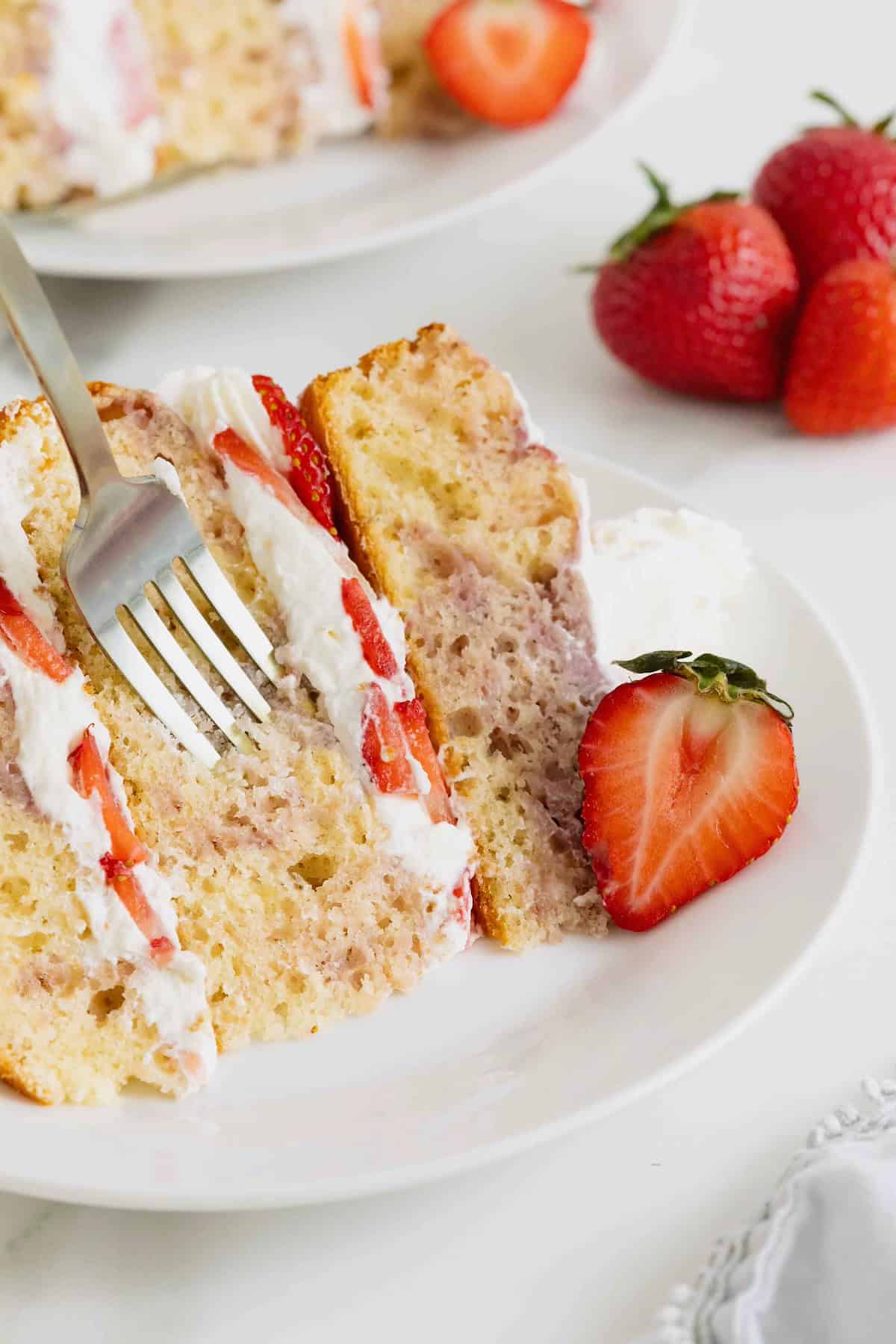 A piece of strawberry swirl layer cake with a fork stuck into it on a white dessert plate.
