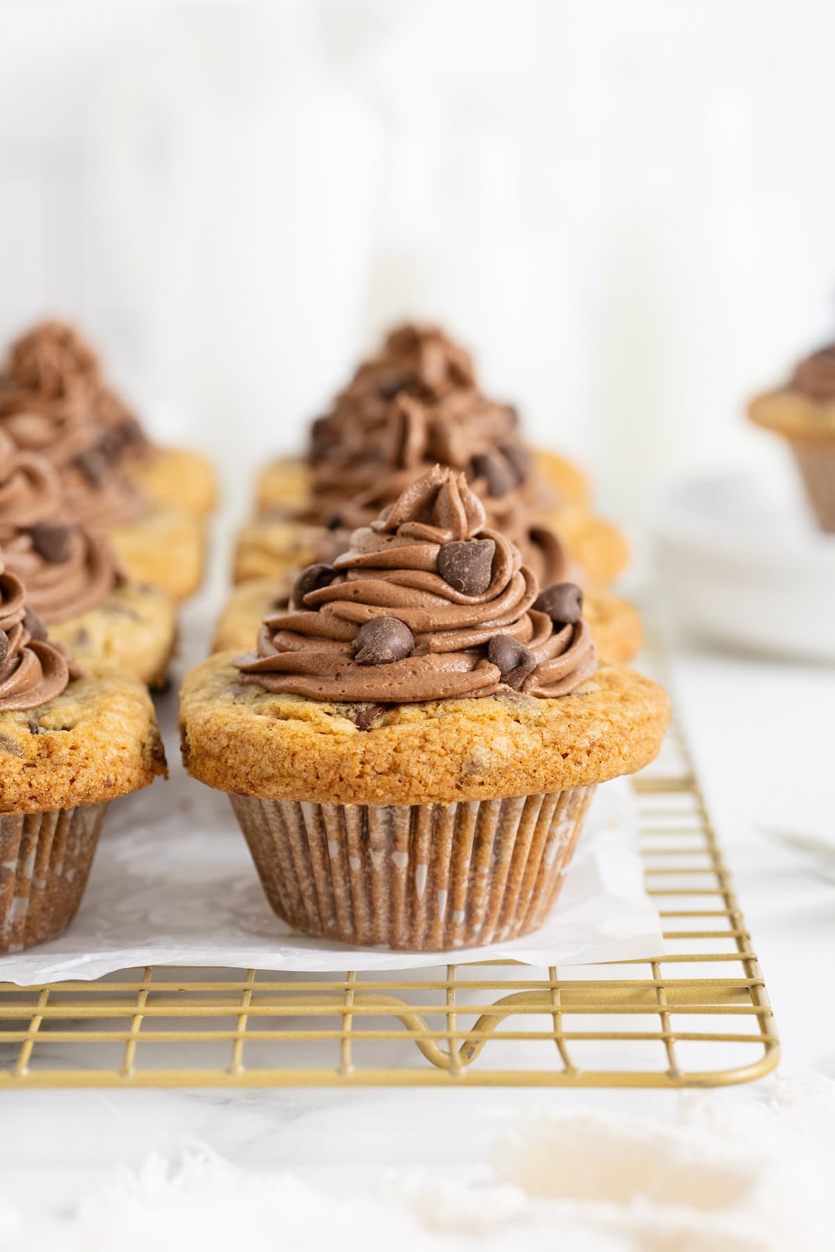 Eight cookie cup cupcakes on a parchment lined wire cooling rack.