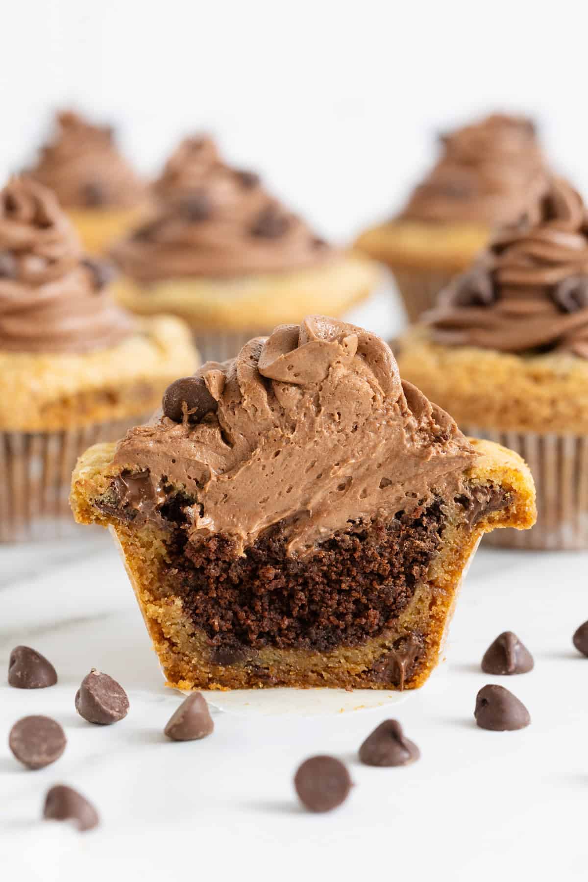 A cookie cup cupcake cut in half on a white marble counter surrounded by chocolate chips.