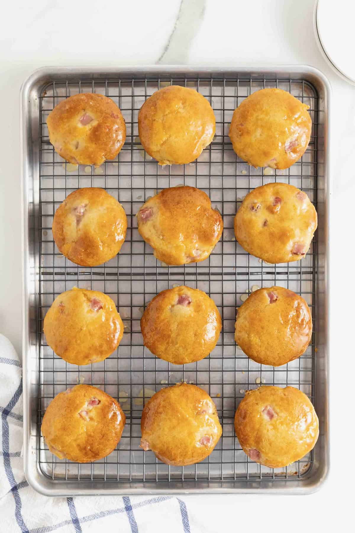 Twelve honey glazed ham muffins on a metal cooling rack over a baking sheet.