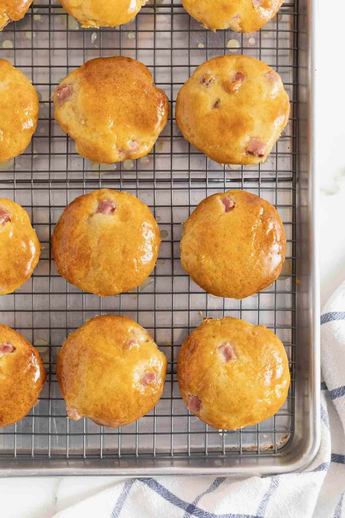 Twelve honey glazed ham muffins on a metal cooling rack over a baking sheet.