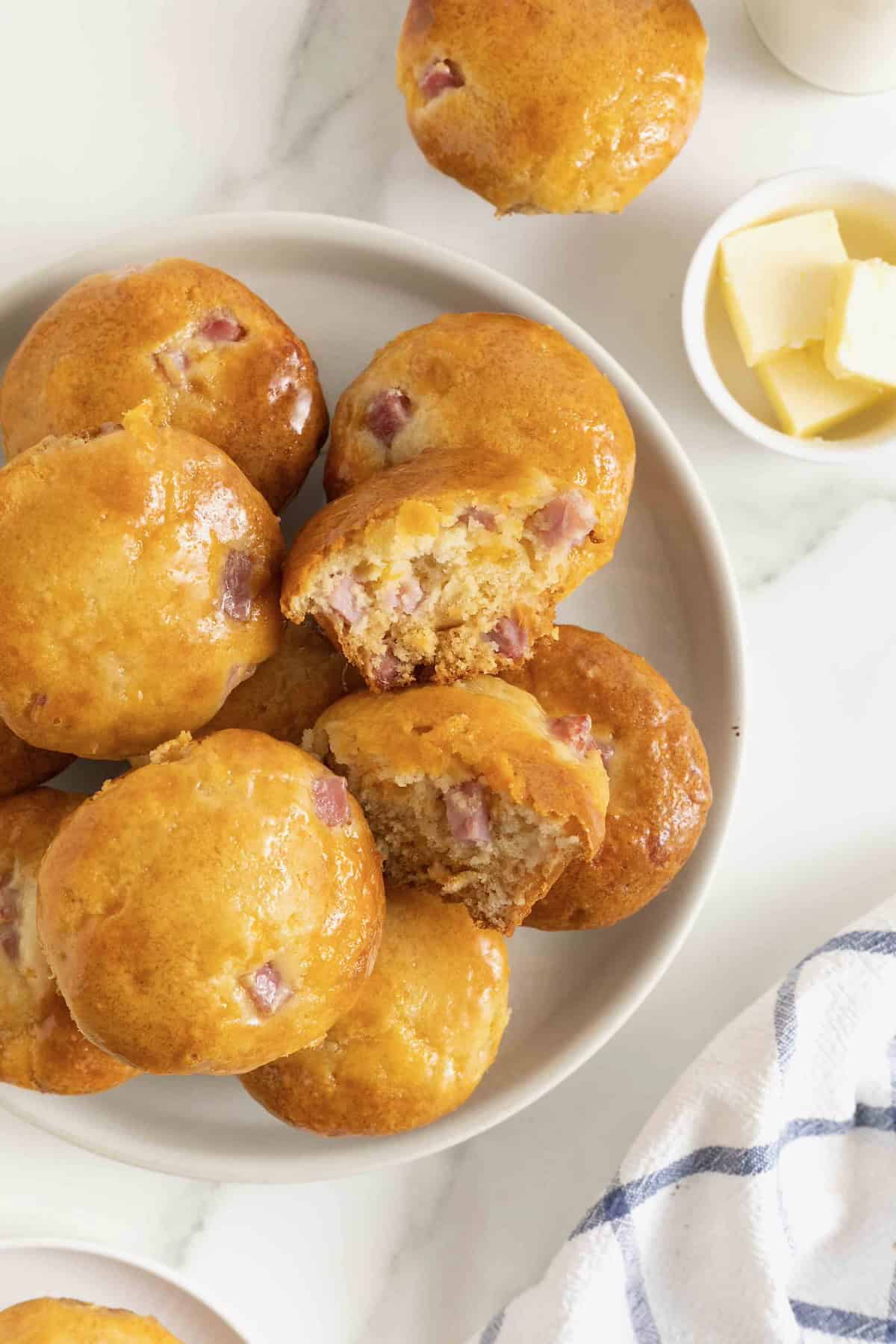 A white platter of honey glazed ham and cheddar muffins. one of the muffins is cut in half to show the inside.