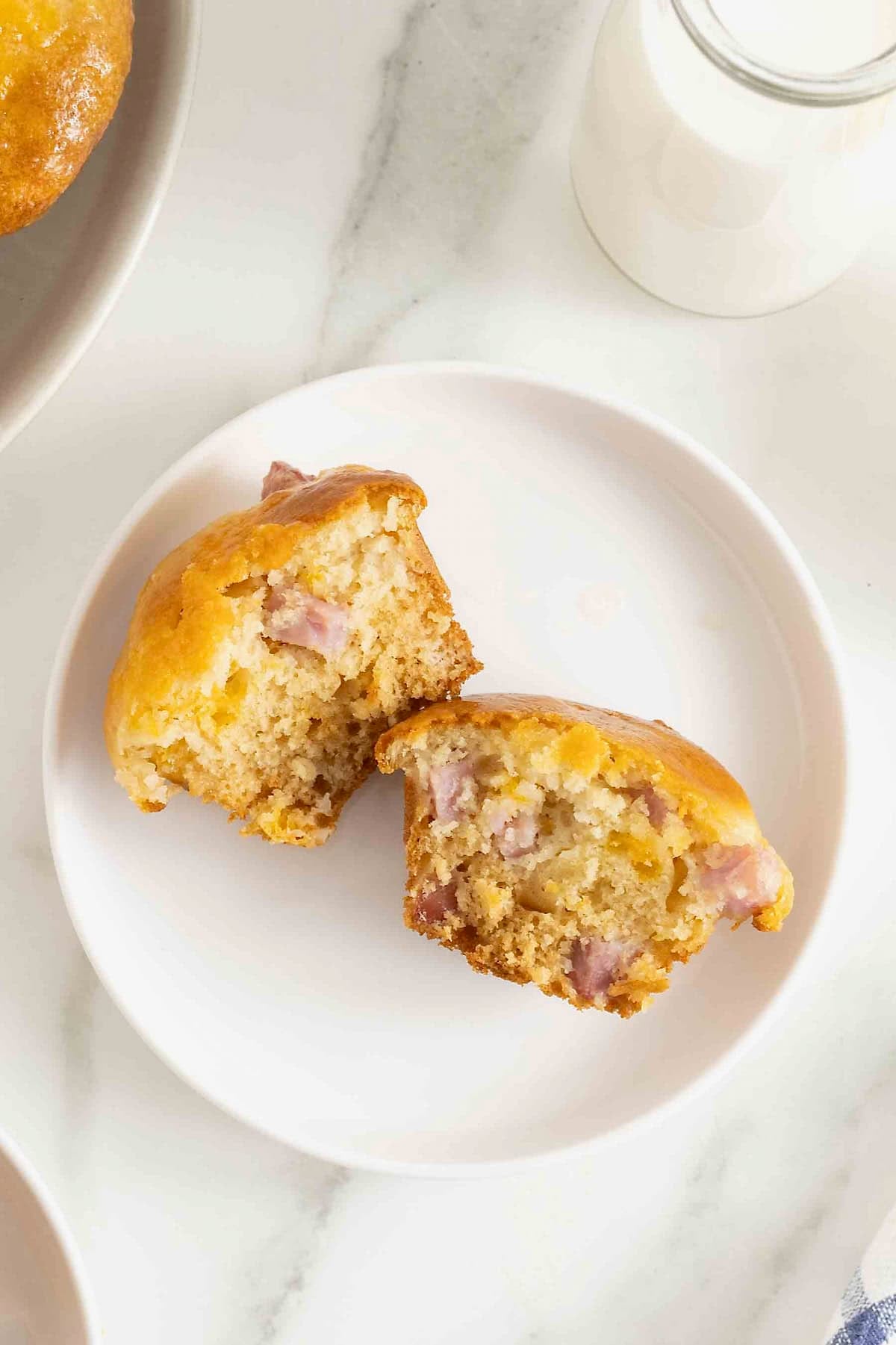 A ham and cheddar muffin cut in half on a white plate.