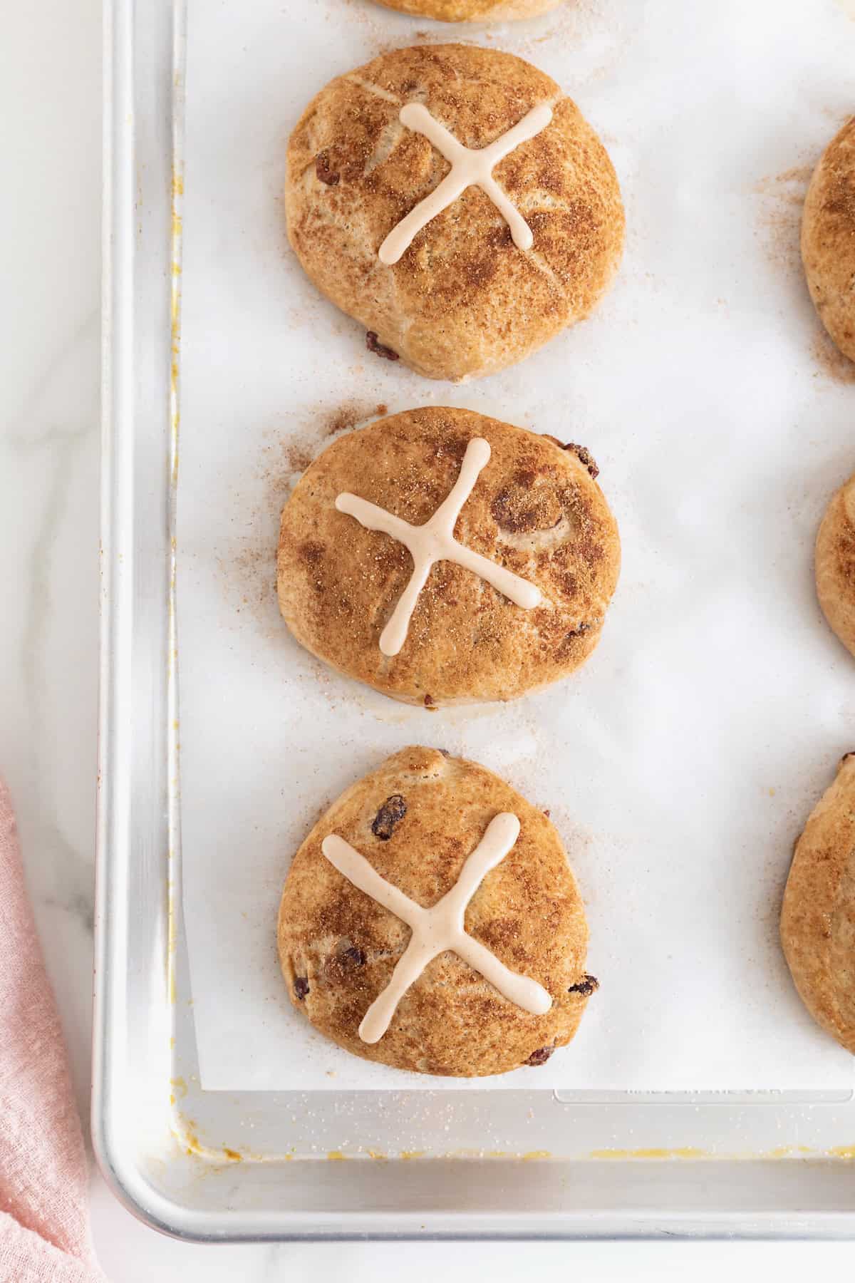 Six hot cross buns on a parchment lined baking sheet.