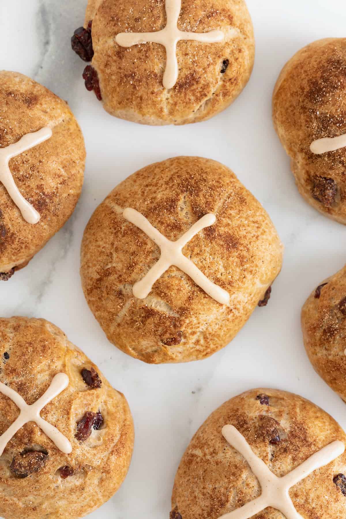 Seven hot cross buns with cranberries on a white marble counter.