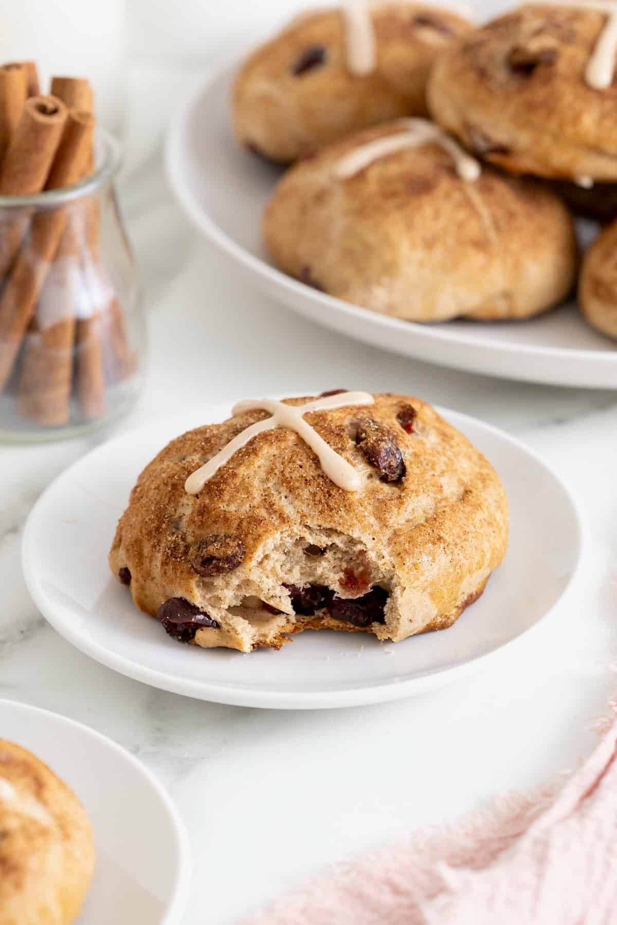 A cinnamon sugar cranberry hot cross bun on a white plate. The bun has a bite out of it.