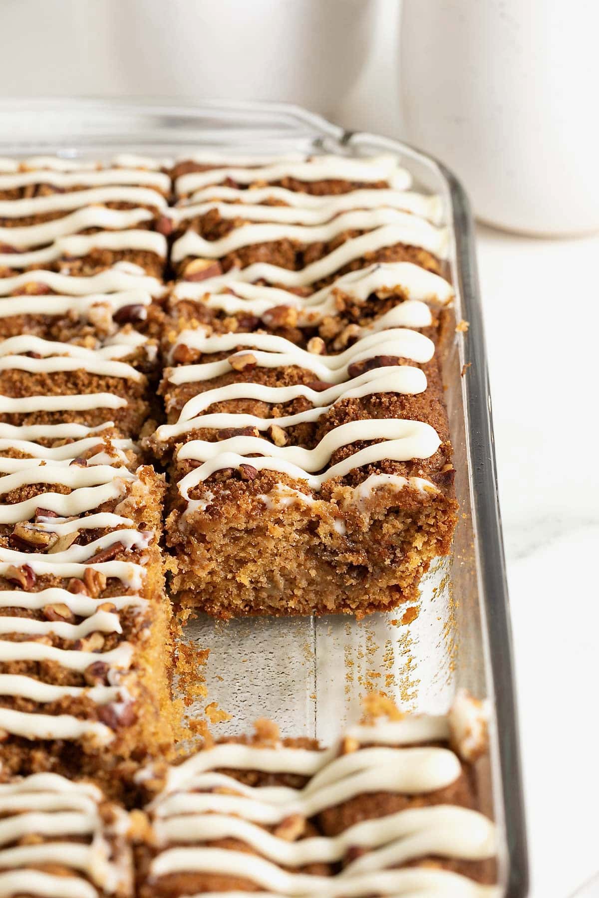 A glass baking dish of coffee cake with a cream cheese drizzle.