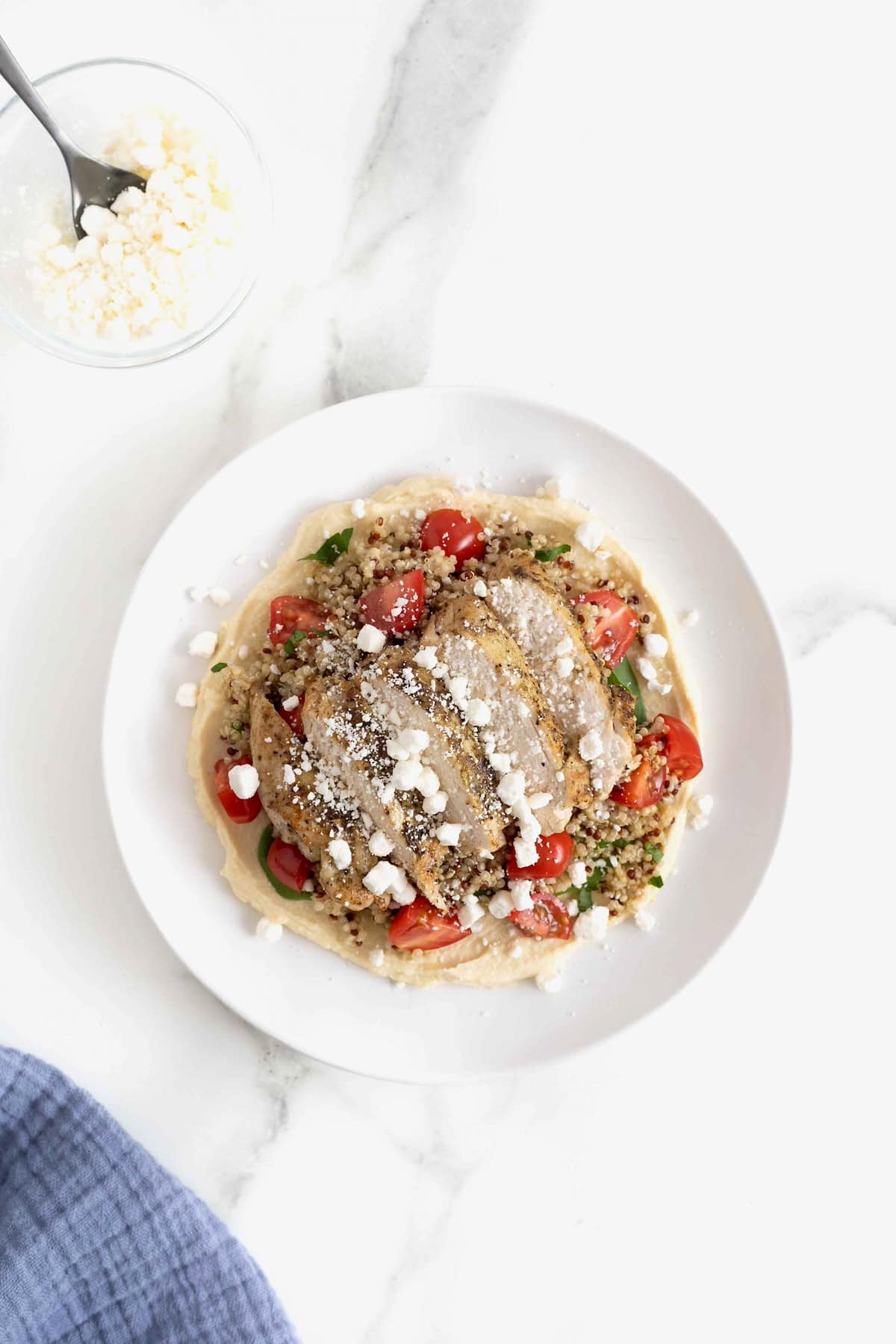 A hummus and quinoa salad with chicken, tomatoes and feta on a white salad plate.
