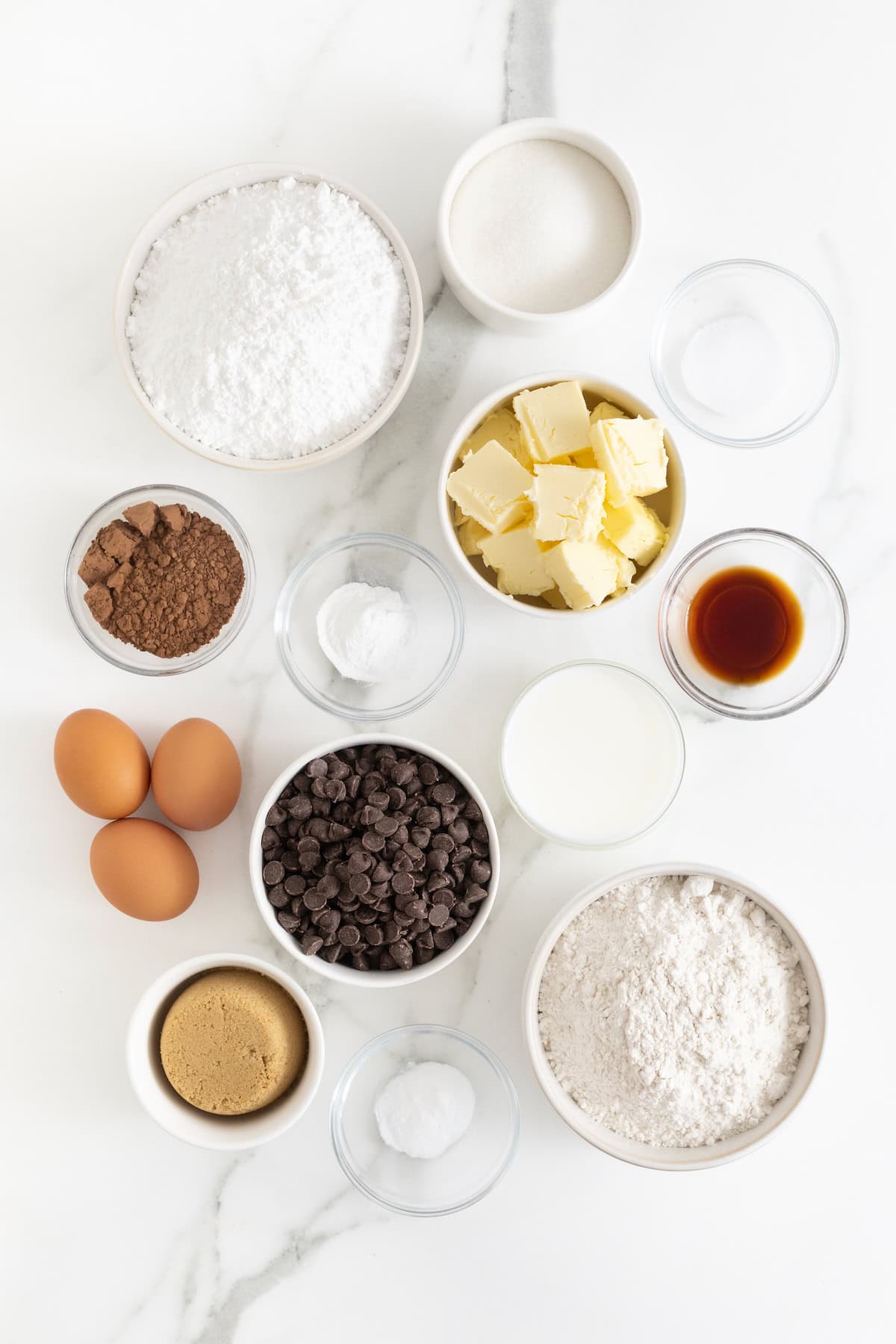 Ingredients to make cookie cup cupcakes in small glass dishes on a white marble counter.
