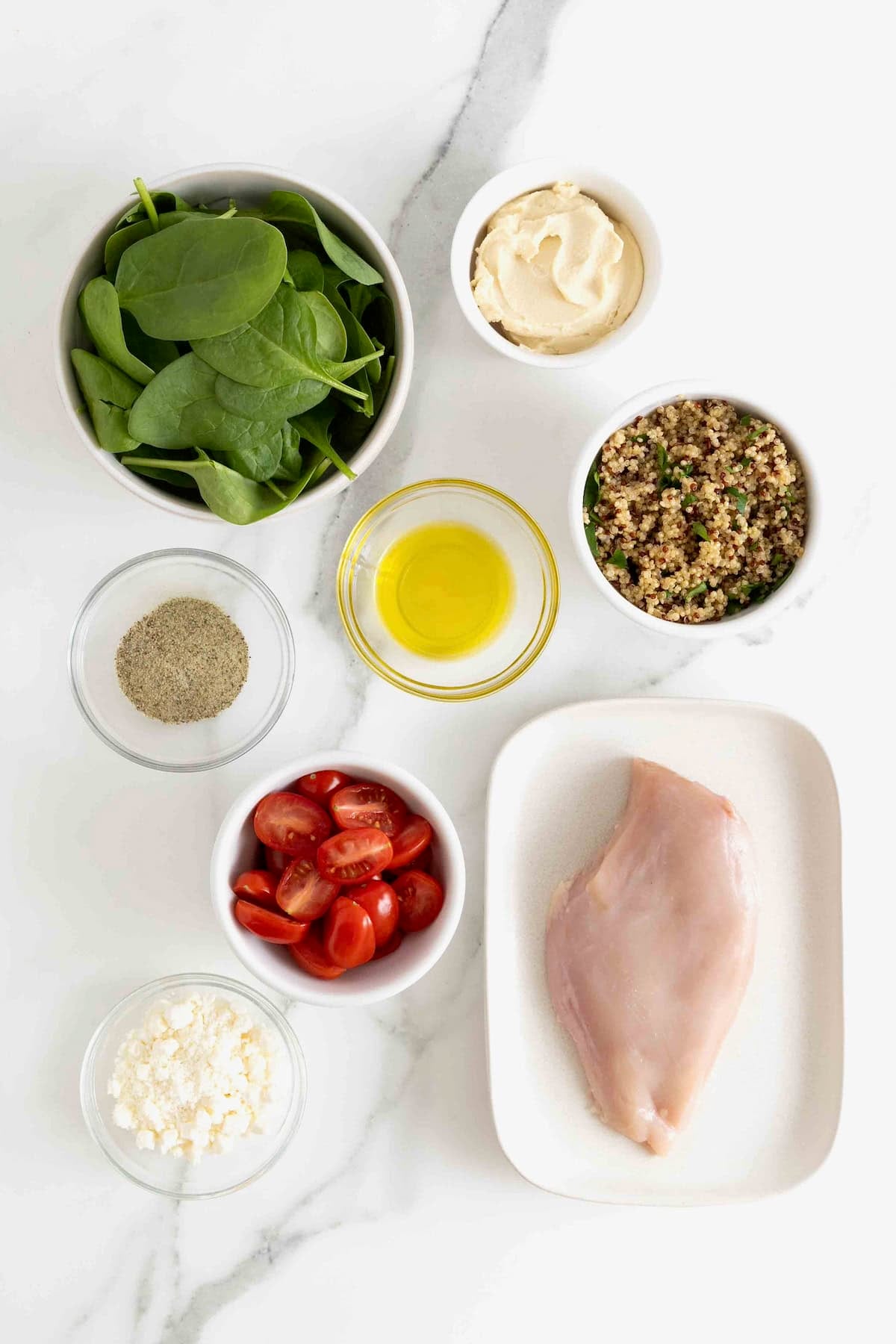 Ingredients for quinoa hummus salad with chicken in small glass dishes on a white marble counter.