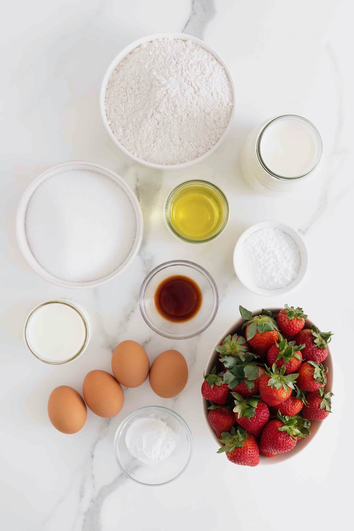 Ingredients to make a strawberries and cream swirl cake in small glass dishes on a white marble counter.