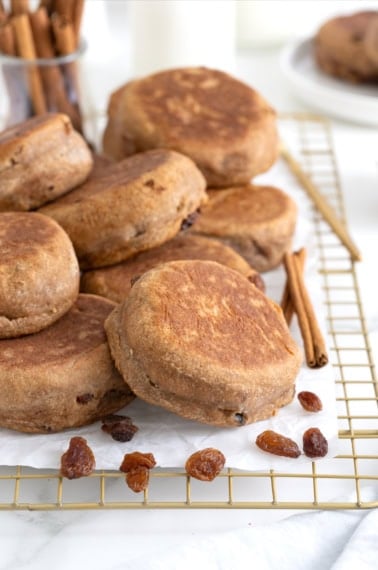 A pile of cinnamon raising English muffins on a parchment lined cooling rack.
