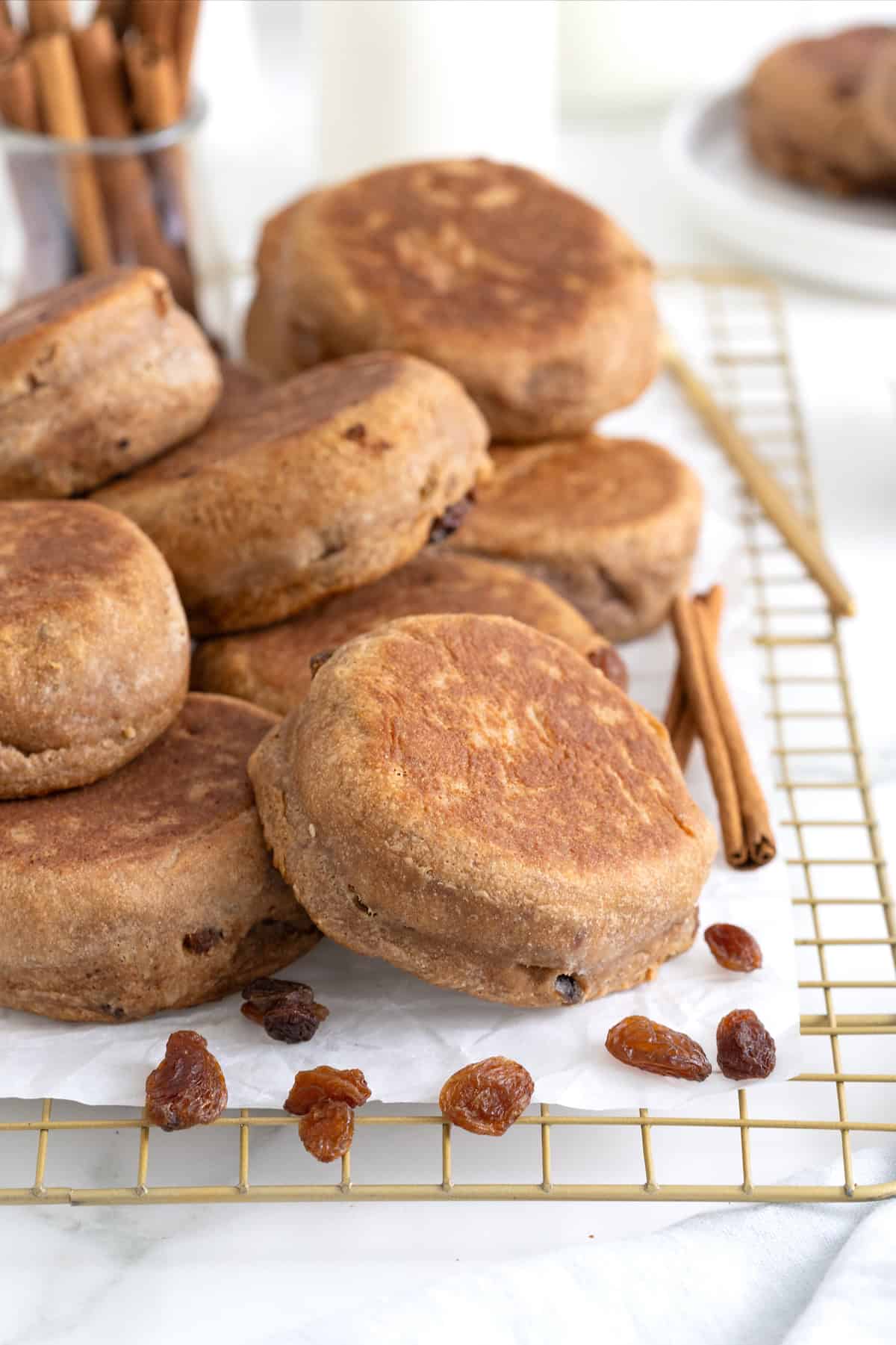 A pile of cinnamon raising English muffins on a parchment lined cooling rack.
