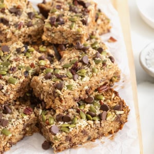 A pile of dark chocolate and coconut granola bars with chopped nuts and seeds.
