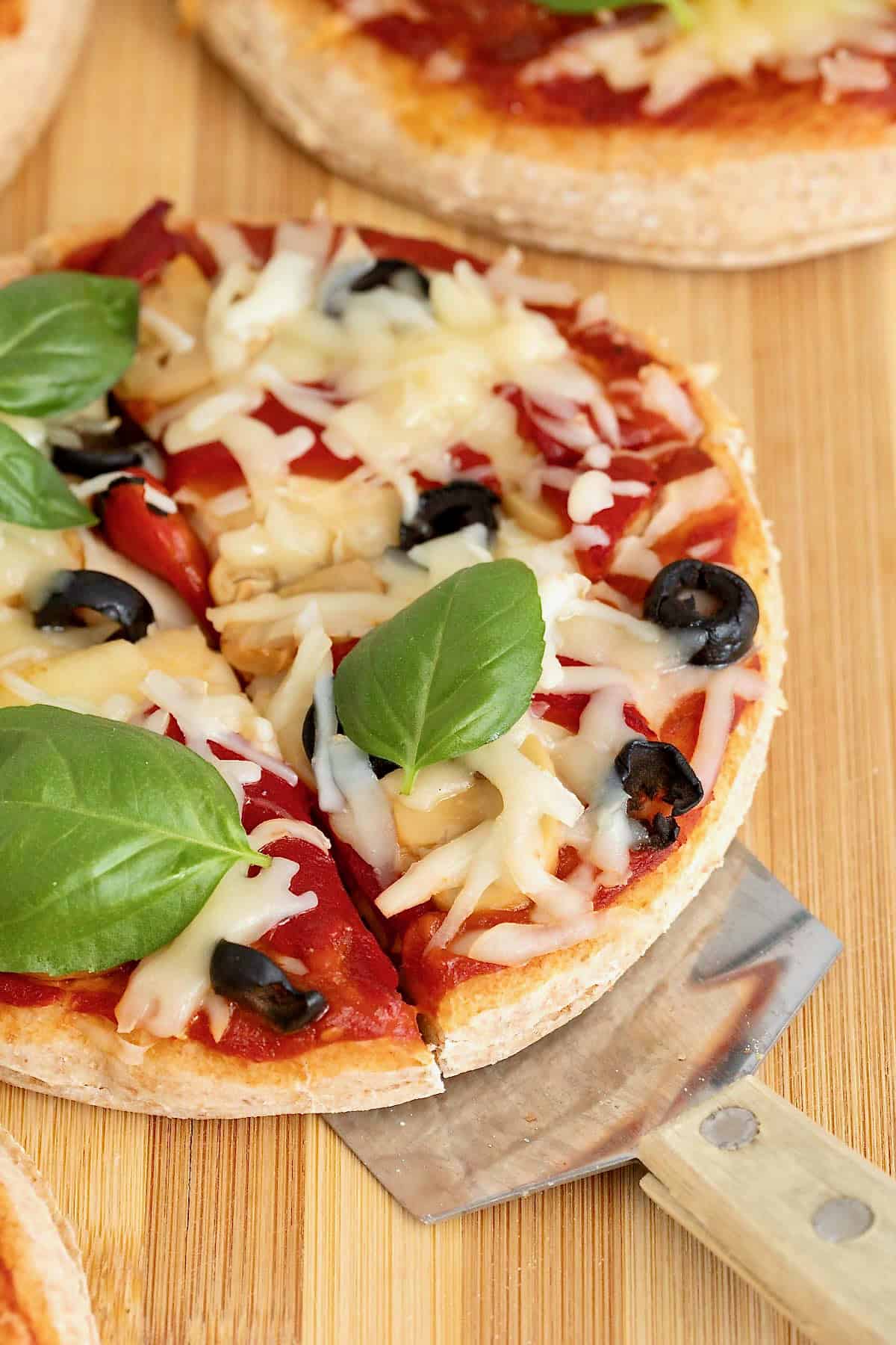 A personal size pizza with a whole wheat crust topped with fresh basil and shredded white cheese on a wooden cutting board.
