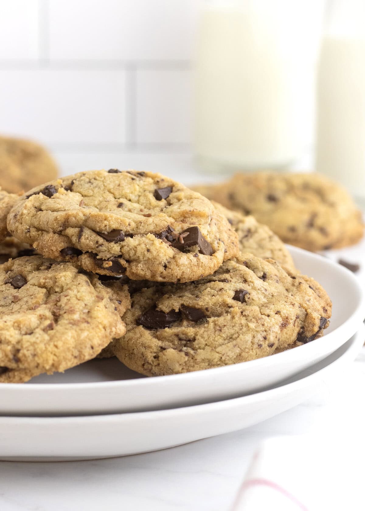 Chocolate chip cookie son a white plate with a glass of of milk in the background.