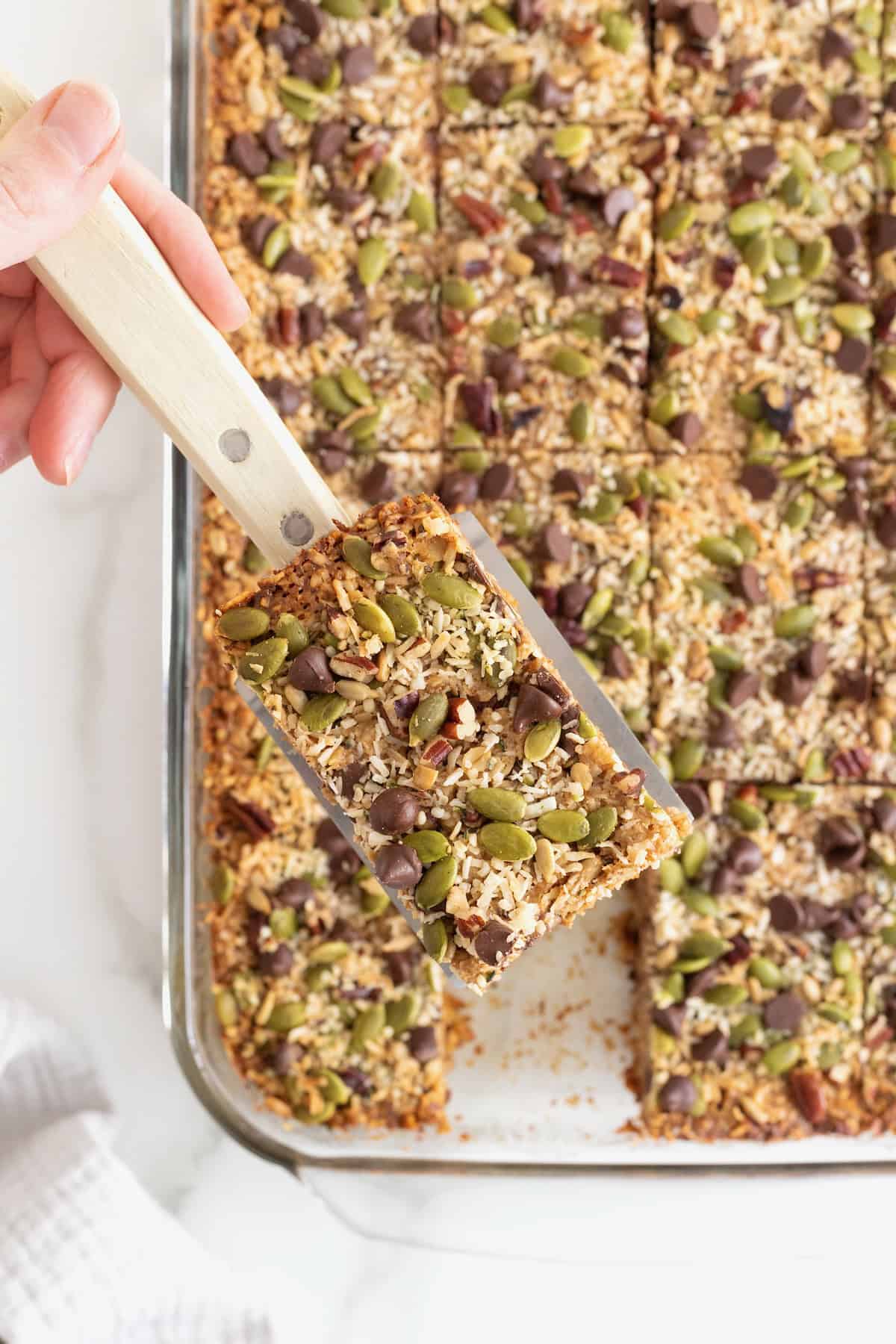 A spatula lifting a granola bar from a glass baking dish.