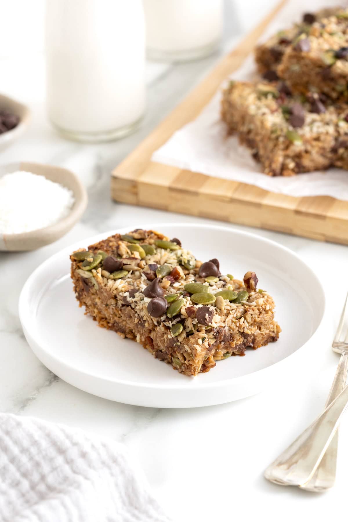 A granola bar topped with coconut and dark chocolate chips on a white rimmed plate.
