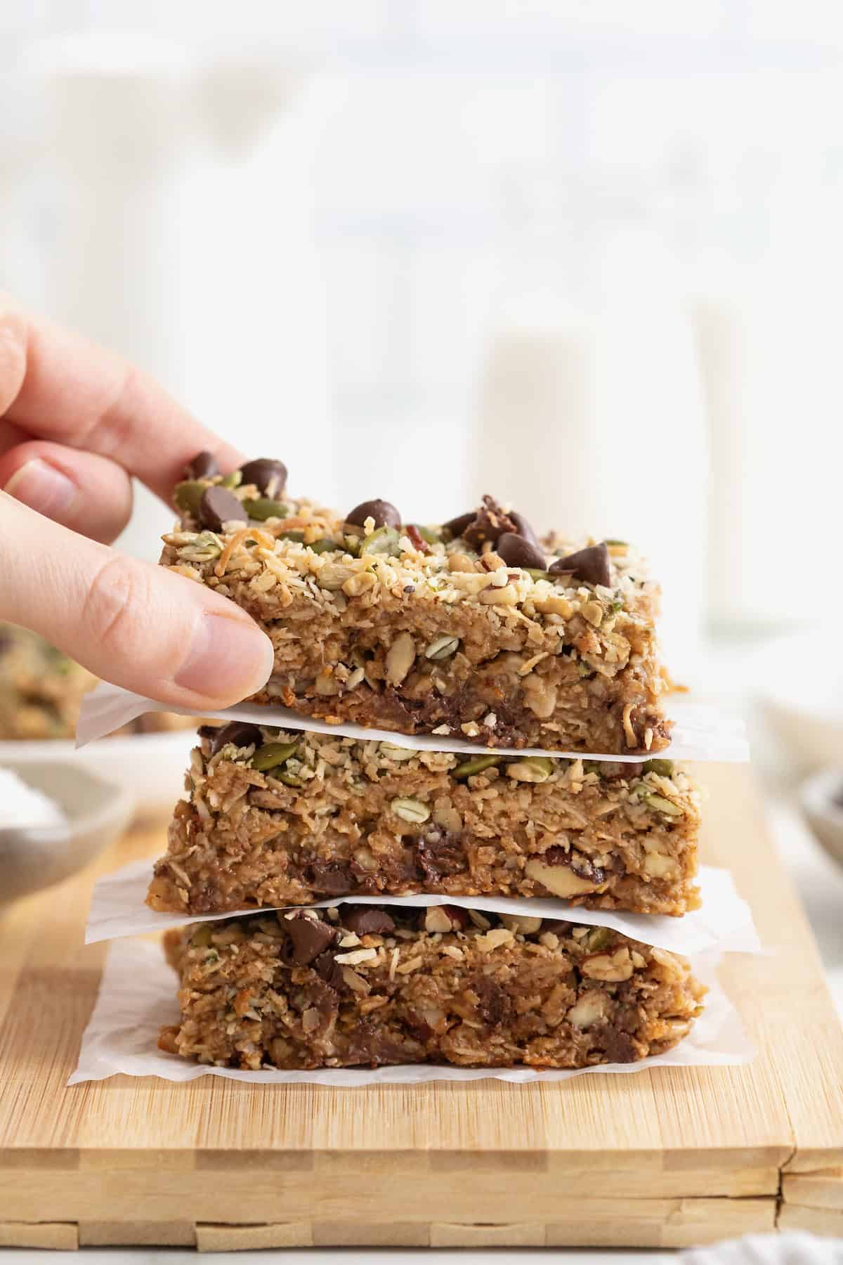 A stack of three coconut chocolate chip granola bars on a wooden cutting board.