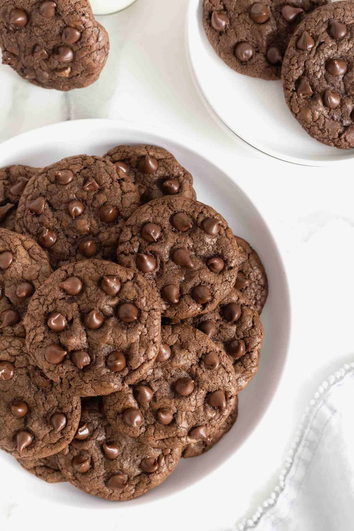 A large white plate of chocolate chocolate chip cookies on a white marble counter.