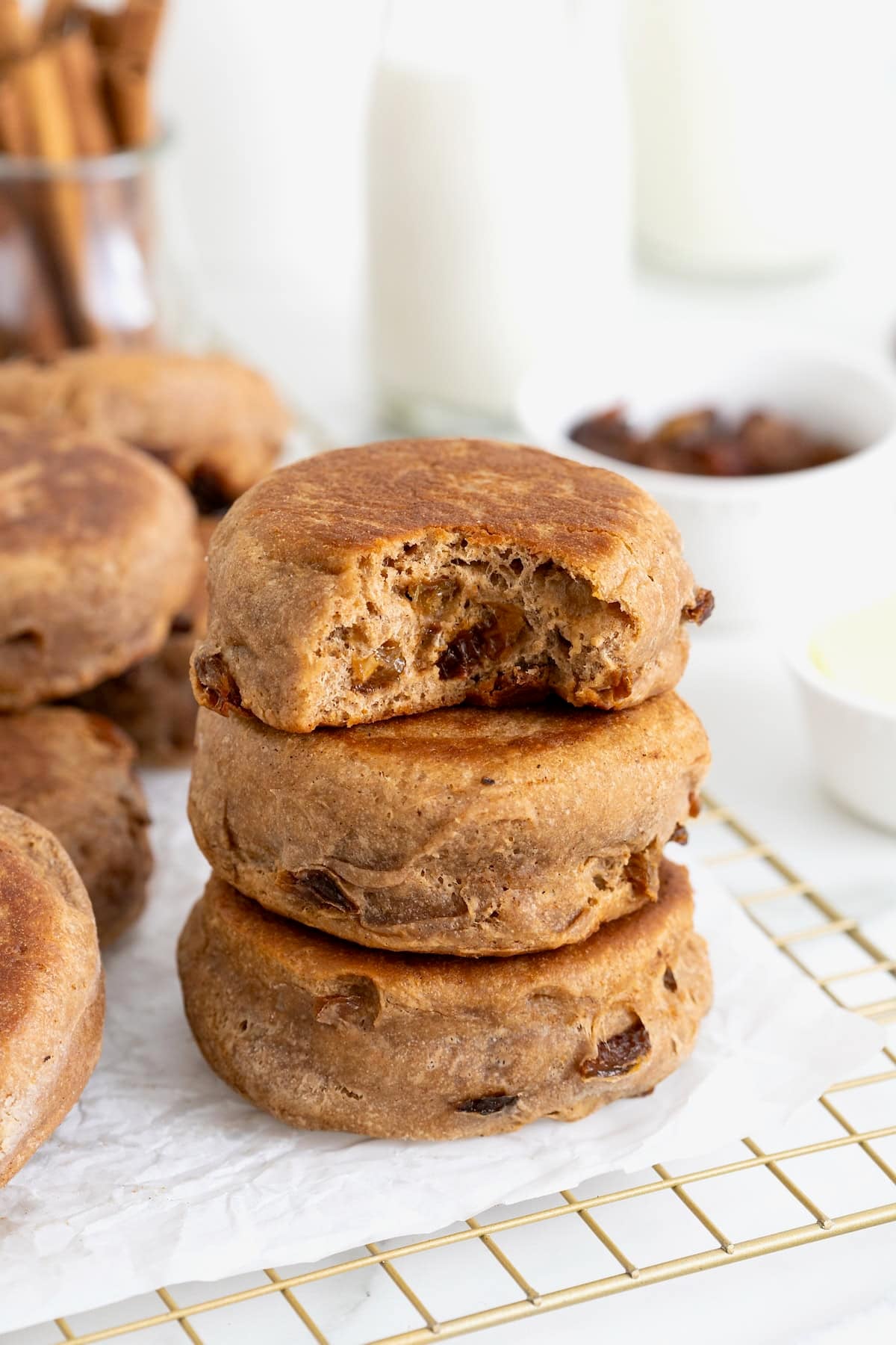 A stack of three cinnamon raisin English muffins on a parchment lined cooling rack.