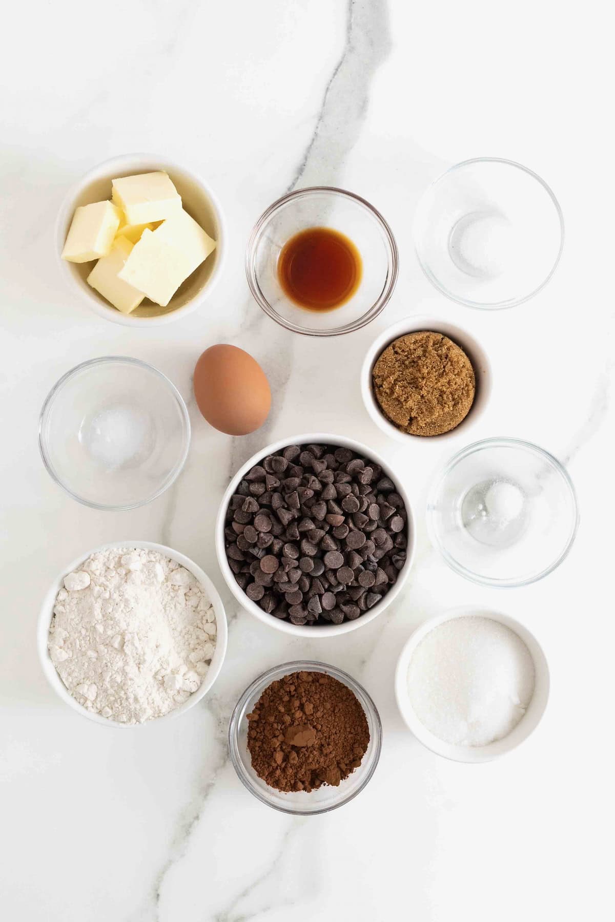 Ingredients to make Chocolate Chocolate Chip Cookies (double chocolate cookies) in small glass dishes on a white marble counter.