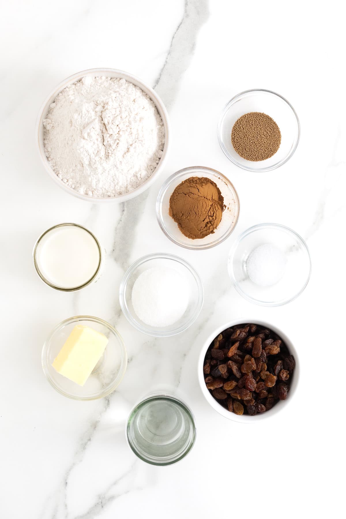 Ingredients to make cinnamon raising English muffins in small glass dishes on a white marble counter.