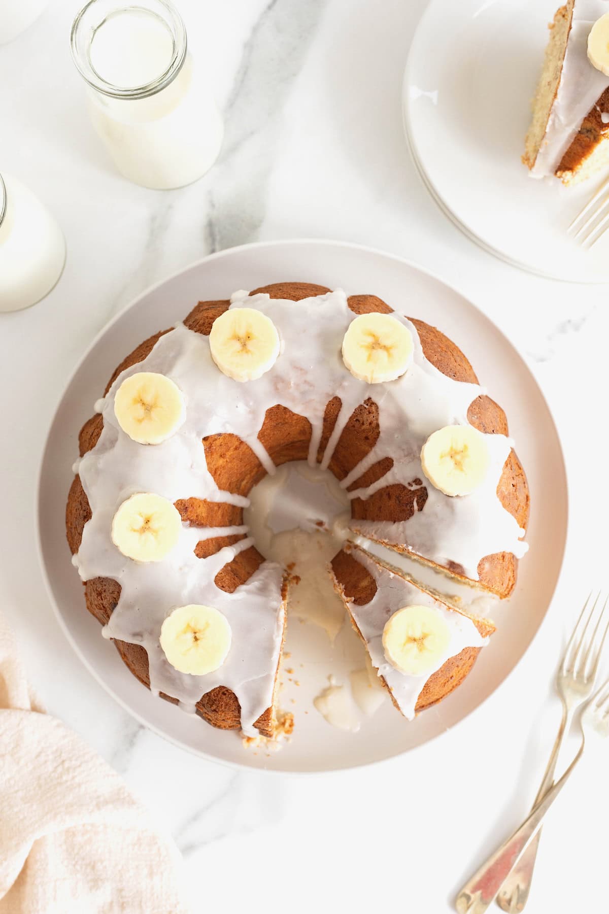 Seen from above, a glazed pound cake garnished with banana slices on a white serving plate.