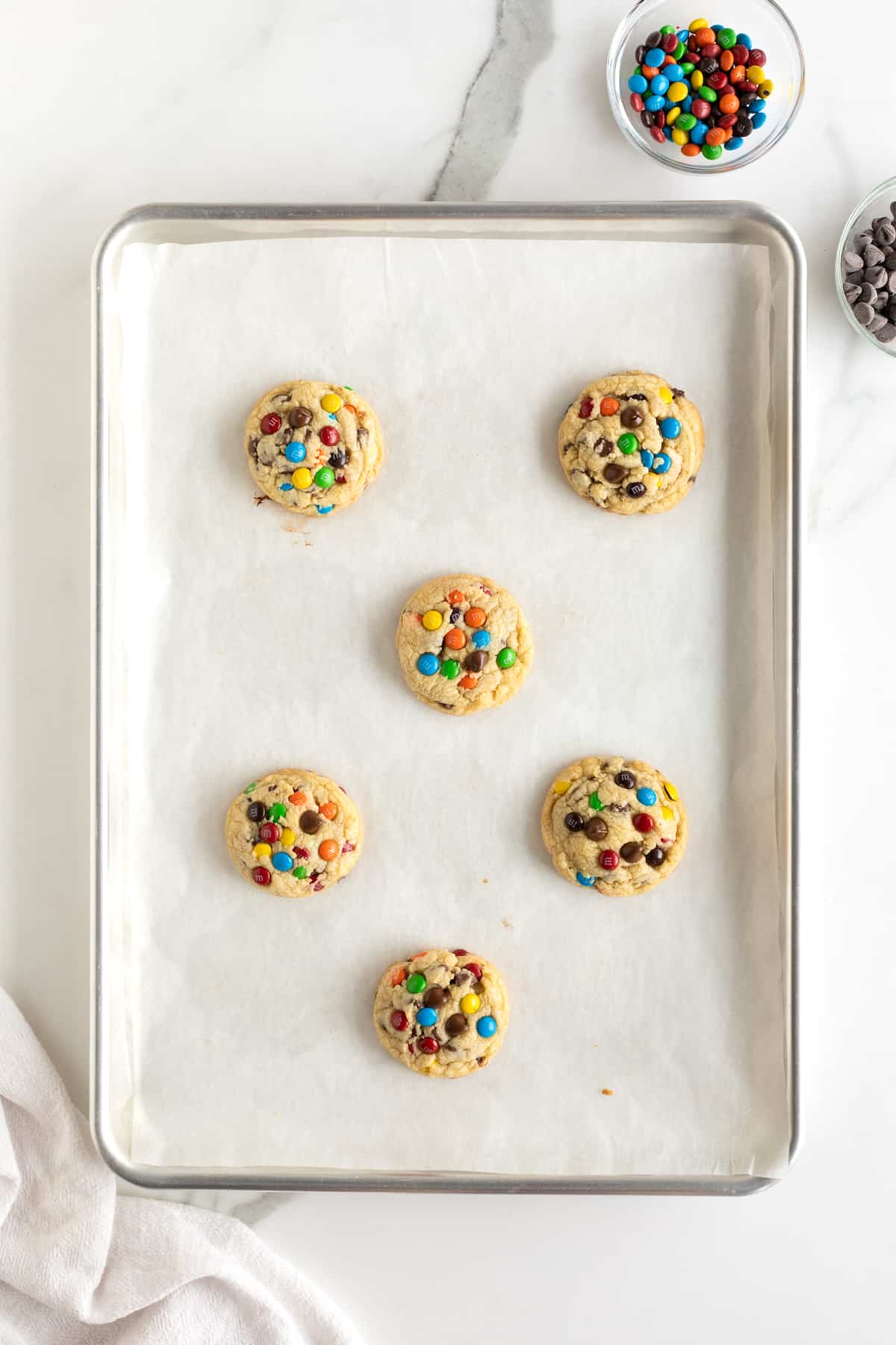 Baked M&M chocolate chip cookies on a parchment lined baking sheet.