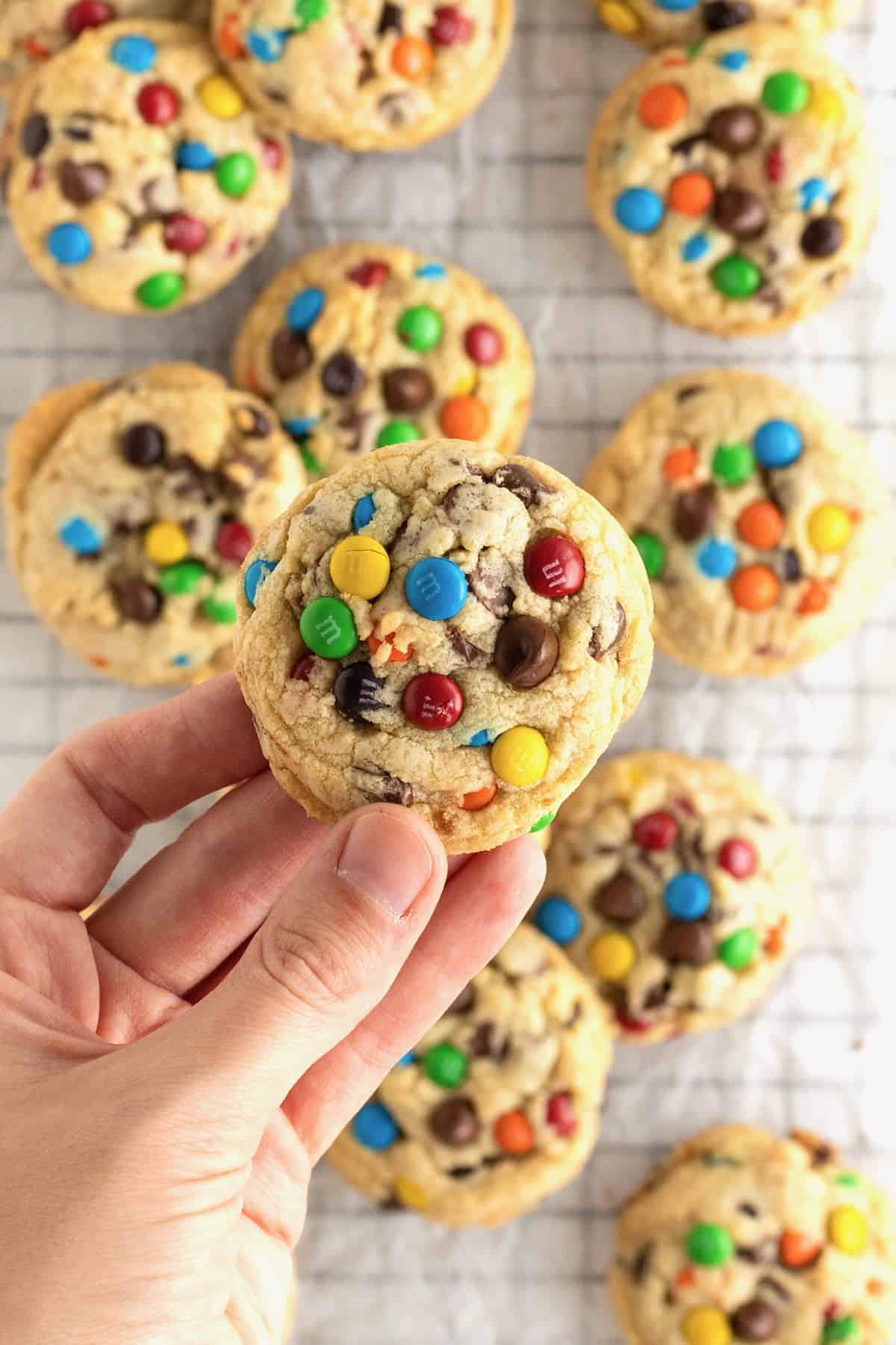A hand holding a cookie with cookies with M&Ms and chocolate chips in it.